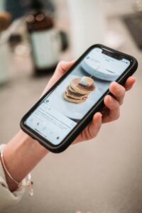 Hand holding a smartphone displaying a pancake recipe on a social media app.